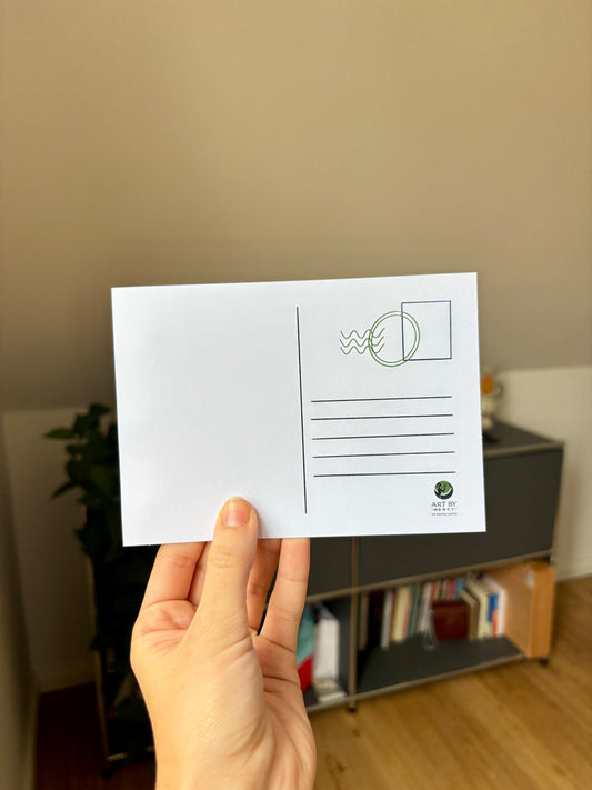 Hand holding a white postcard with a logo against a blurred indoor background