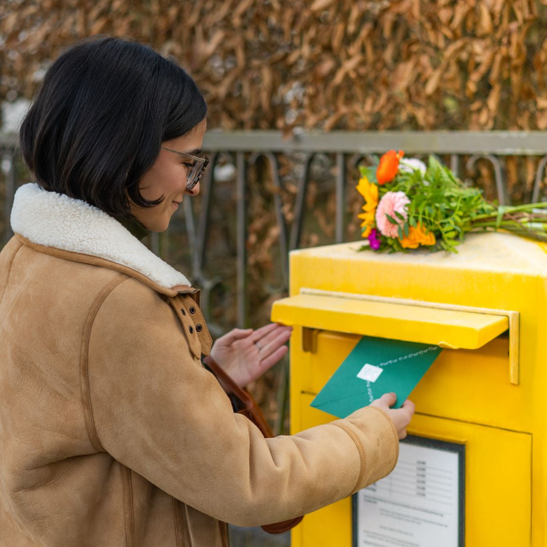 Woman placing a letter into a yellow mailbox with flowers on top