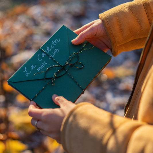Person holding a green envelope with string, blurred autumn background