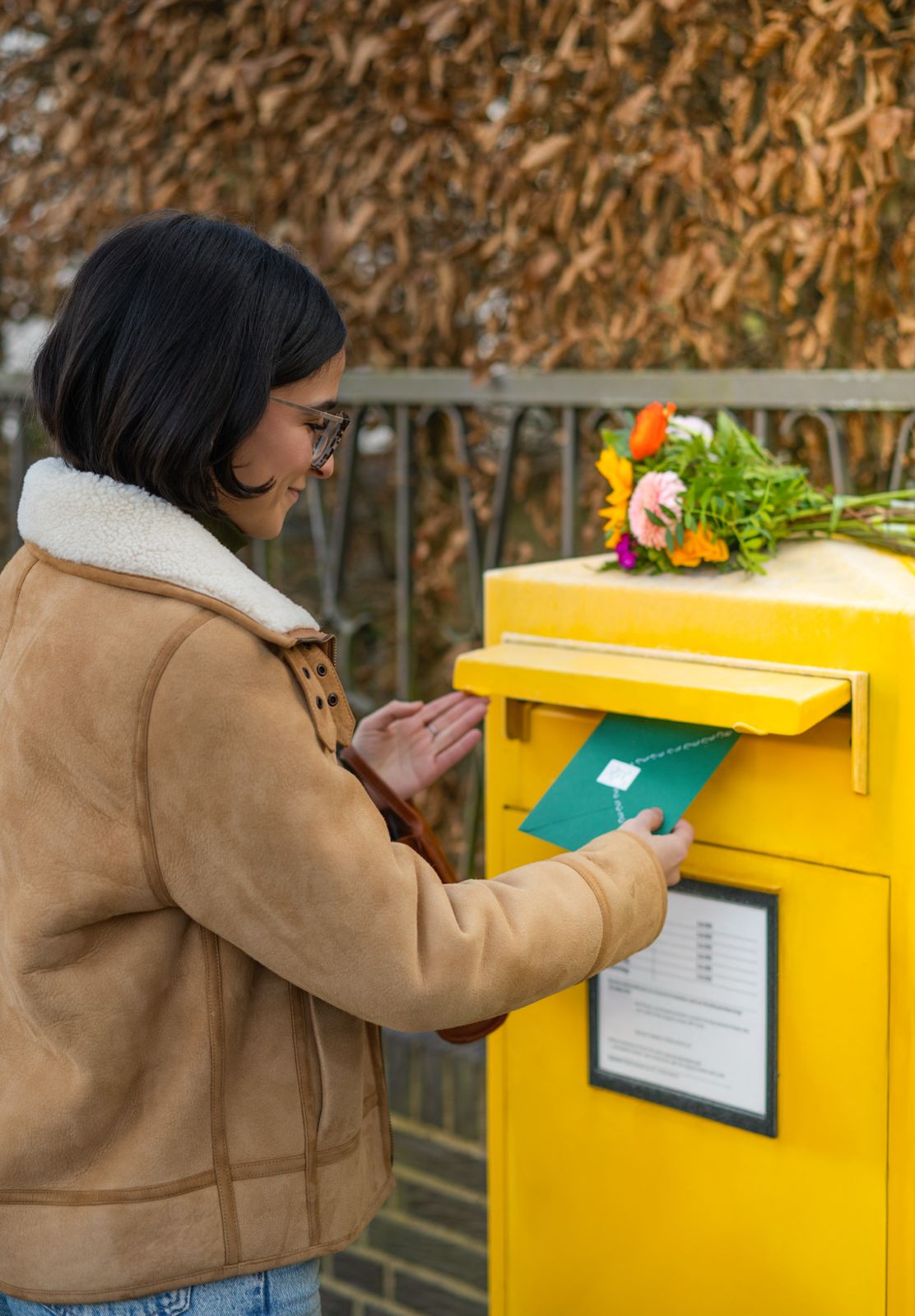 Person placing a letter into a yellow mailbox with flowers on top