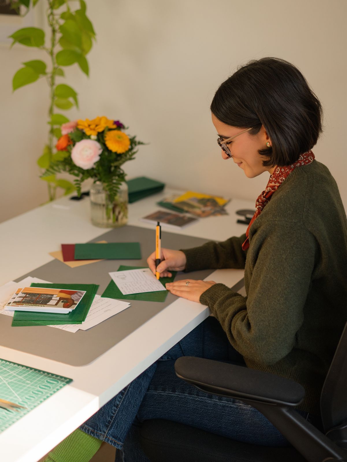 Person sitting at a table with stationery items and a flower arrangement.